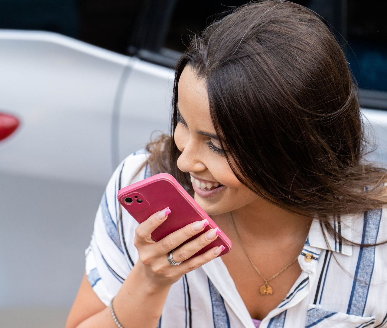 High angle view of a smiling young woman talking on her mobile phone while standing outside by her care