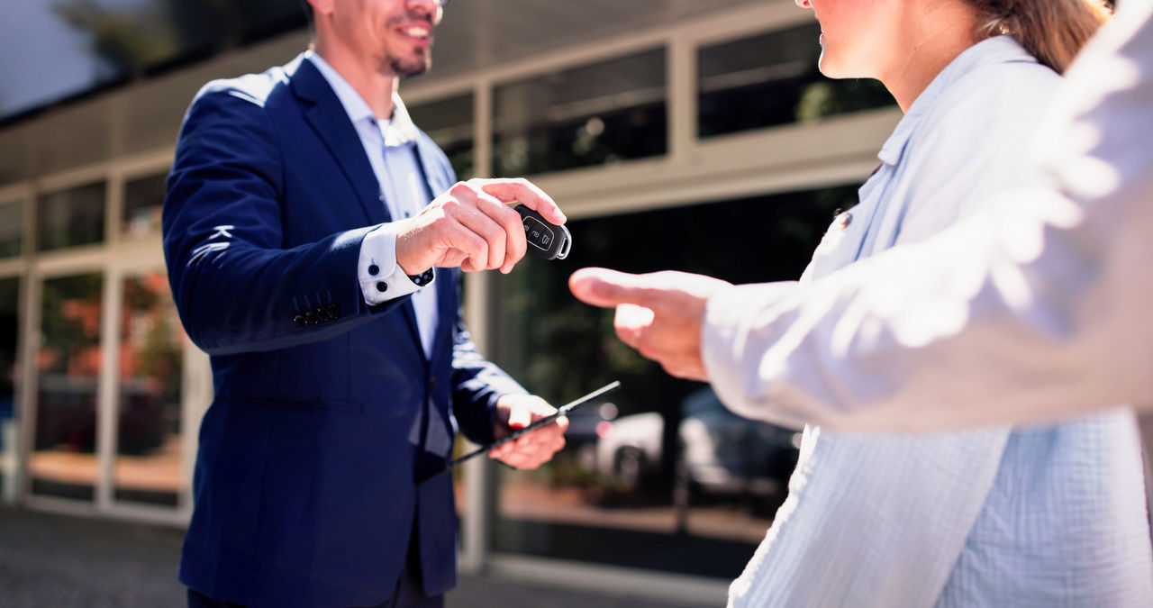 Smiling Hispanic Salesman Successfully Handing Over Keys to New Car Owners at Local Dealership During Business Hours.